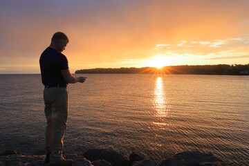 Middle-aged man checks his picture of the sun rising over the water