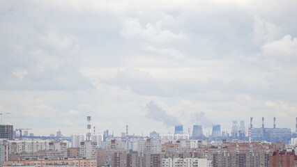 City skyline with residential buildings and industrial area withк chimneys and cooling towers emitting smoke under cloudy sky
