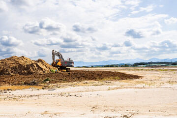 Yellow excavator with a hydraulic breaker attachment working at a construction site on a sunny day....