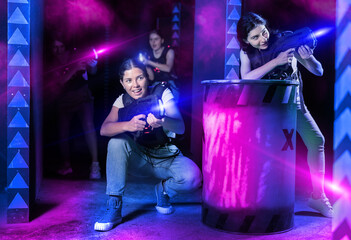 Laser tag players cheerful positive smiling girls playing in teams in dark laser tag room