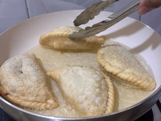 A close-up shot of several jalangkote pastries being fried in a pan. The image captures a pair of tongs flipping a pastry, showcasing the delicate and crispy cooking process.