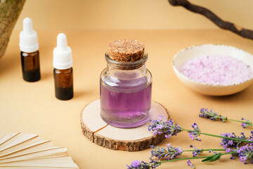 Glass jar with purple hydrolat, essential oil bottles, lavender flowers and bath salt on beige background. Aromatherapy concept. Closeup