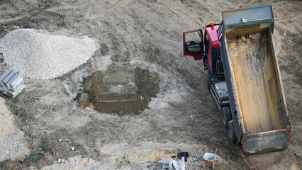 Aerial view of construction site with a red dump truck unloading sand and gravel, industrial work in progress, building foundation preparation, heavy machinery and raw materials on ground.  © belavinstock