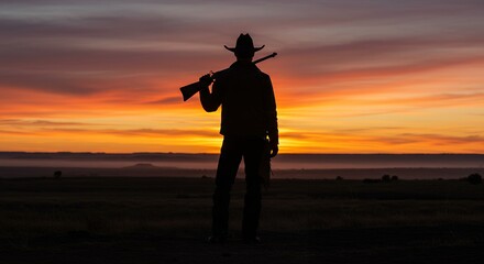 Silhouette of person with rifle at sunset