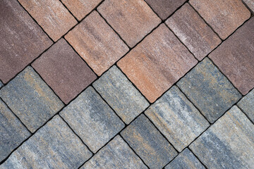 Colorful paving stones arranged in neat diagonal pattern showcasing contrast between warm brown and cool gray tones. Concept of paving, texture, construction background