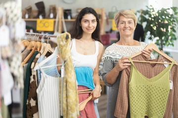 Woman customer with senior mother making choice and elect something summer clothes in store, and...