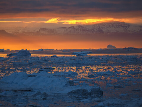 Vibrant Arctic sunset with fiery red sky reflecting over frozen sea and drifting icebergs.