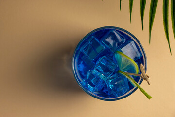 Colorful blue cocktail in a glass with a slice of lime on a beige background