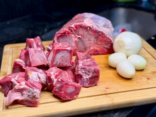 Carne em cubos cortas sobre a mesa com fundo desfocado e cebolas e panela con nivel de agua.