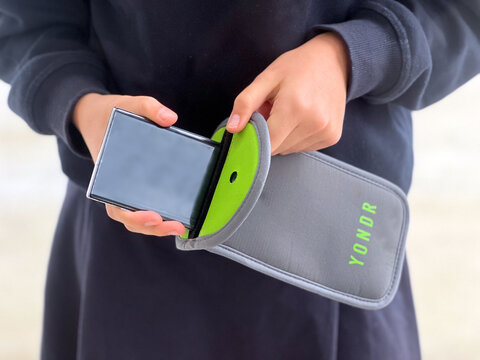 Student using a mobile phone and YONDR lockable phone case pouch