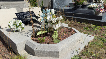 Weathered artificial flowers adorn a grave in a modern cemetery