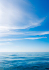 Obraz premium Tranquil seascape featuring calm, reflective water under a clear blue sky with soft, wispy clouds.