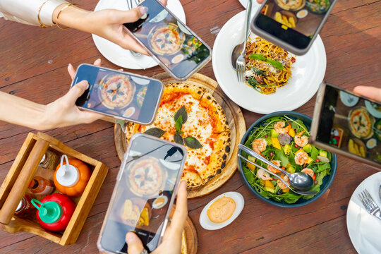 Group of Happy Asian man and woman using mobile phone taking picture food and drink on dining table. People friends enjoy and fun meeting celebration holiday event dinner party together in the garden.