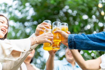 Group of happy diverse Asian millennial people friends enjoy holiday celebration social gathering dinner party in garden evening, drinking beer and toasting glasses together outdoor festive event.