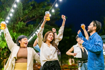 Happy diverse Asian millennial people friends enjoy and fun meeting holiday celebration social gathering dinner party in garden evening, drinking beer and dancing together outdoor festive event.