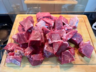 Carne em cubos cortas sobre a mesa com fundo desfocado e cebolas e panela con nivel de agua.