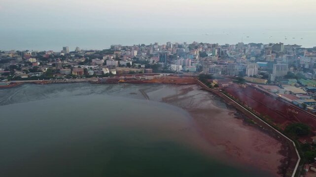 Aerial view of a coastal city with buildings, a beach, and a body of water during daytime Guinea