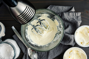 Homemade Cream Cheese Frosting with hand Mixer: Glass mixing bowl of beaten heavy whipping cream,...