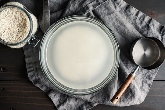 Sticky Rice Soaking in a Glass Bowl: Short-grain glutinous rice soaked in cloudy water in a mixing bowl with a jar of sweet rice nearby