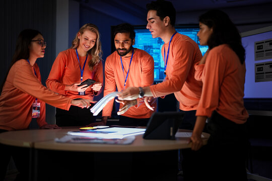 A team of hardware engineers and UI UX designers reviews a new smartphone prototype. They are analyzing the device's ergonomics and the mobile operating system's user flow.