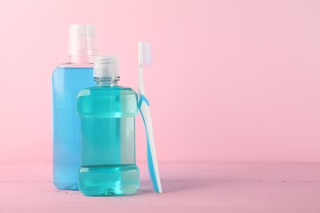 Mouthwash in bottles and toothbrush on pink background, space for text. Oral hygiene