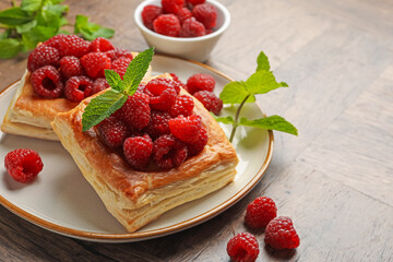Yummy puff pastries with raspberries and mint on wooden table, closeup. Space for text