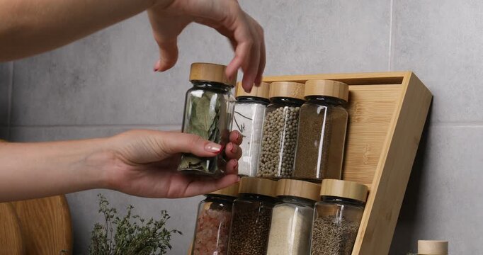 Woman taking bay leaf from glass jar in kitchen, closeup