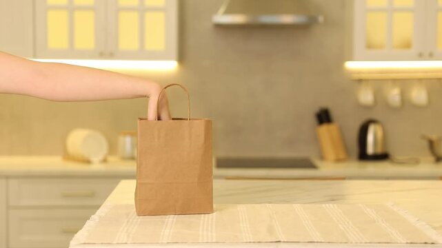 Packaging. Woman taking zucchini and bell pepper out of paper bag at table in kitchen, closeup