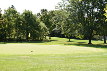 Obraz premium Golf course putting green and partial fairway view showing the goal of sinking a put in the location indicated with the yellow flag and pole.