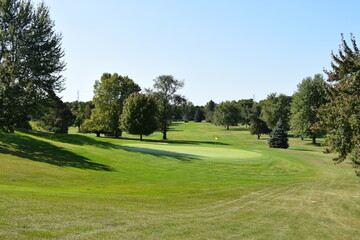 Golf course putting green and partial fairway view showing the goal of sinking a put in the location indicated with the yellow flag and pole.