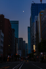 夕暮れ時の大通りとビル街の上に月が光る20250831