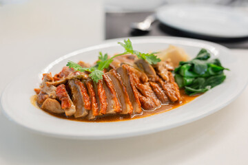Roasted duck with rich brown sauce served on a white plate, garnished with fresh cilantro, vegetables, and pickled ginger. Asian Food culture.