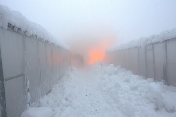 Snow-covered pathway between misty structures