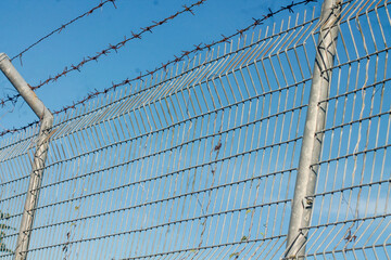 Closeup of a metal chain link fence with a clear blue sky background.	
