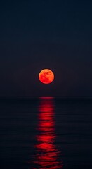 A dramatic, vibrant red moon hangs over a dark, reflective sea, casting a spectral glow on the water's surface.