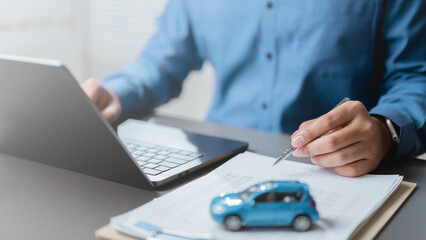 Businessman working with laptop and documents with car model on desk, symbolizing car loan, vehicle...