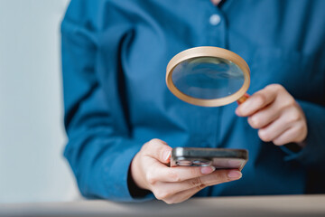 Close-up of a person using a magnifying glass to examine a smartphone, symbolizing digital analysis, online security, and modern technology research.