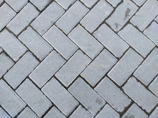A close-up view of a gray paver block surface laid in a herringbone pattern. The rough texture and clear grout lines create a uniform, geometric design ideal for backgrounds.