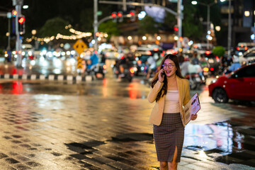 Businesswoman walking and talking on phone in rainy city at night