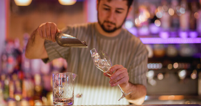 Preparing cold drink. Barkeeper workspace. Man pouring ice cubes with scoop in wineglass. Professional worker making refreshing beverage.