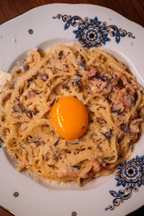 Served pasta. Traditional italian dish. Appetizing noodles with egg yolk on plate. Tasty carbonara recipe with grated cheese seasoning.