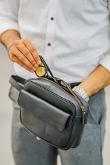 A man's hand in a white shirt is putting a smartphone into a black leather handbag.
