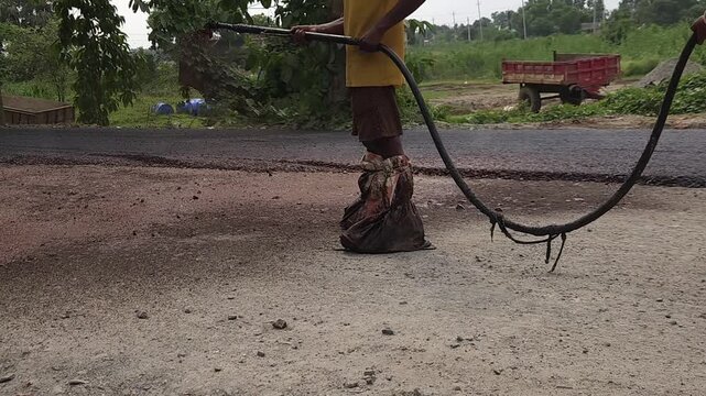 Road construction works going on in slow otion. Indian men working road maintenance. Road construction site in India. Road construction works going on in slow motion. Indian worker spraying primer.