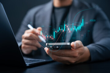 Stock market investment concept, businessman using smartphone and laptop to analyze digital candlestick charts, mobile stock trading, financial technology and real-time analysis.
