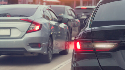 Rear side of black car with effect from brake light. Traffic jam in the city. Many cars are parked in a row on the asphalt road.