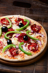 Pizza with chorizo ​​sausage, mozzarella cheese, green pepper and black olives. Rustic wooden background. Soft focus.	