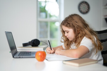 Child learning online with laptop at home. Kid studying using laptop in classroom. Kid student doing homework during online lesson. Kid focused on laptop in homeschooling. Student at desk e-learning.