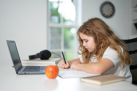 Child learning online with laptop at home. Kid studying using laptop in classroom. Kid student doing homework during online lesson. Kid focused on laptop in homeschooling. Student at desk e-learning.