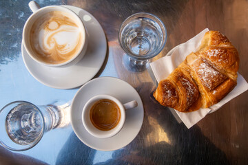 Stockholm, Sweden A stainless tabletop with a cappuccino and an espresso coffee and a sugary croissant.