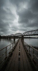 A weathered wooden walkway stretches towards a large metal bridge under a brooding sky.